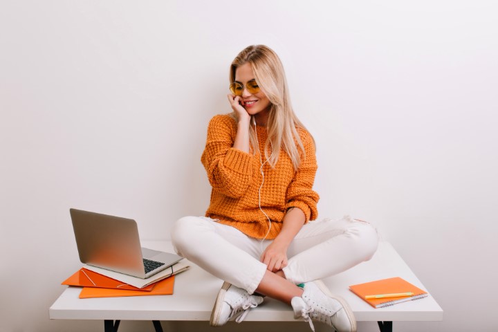 superbe mannequin féminin en tenue décontractée se relaxant sur une table avec un sourire regardant un écran d'ordinateur portable