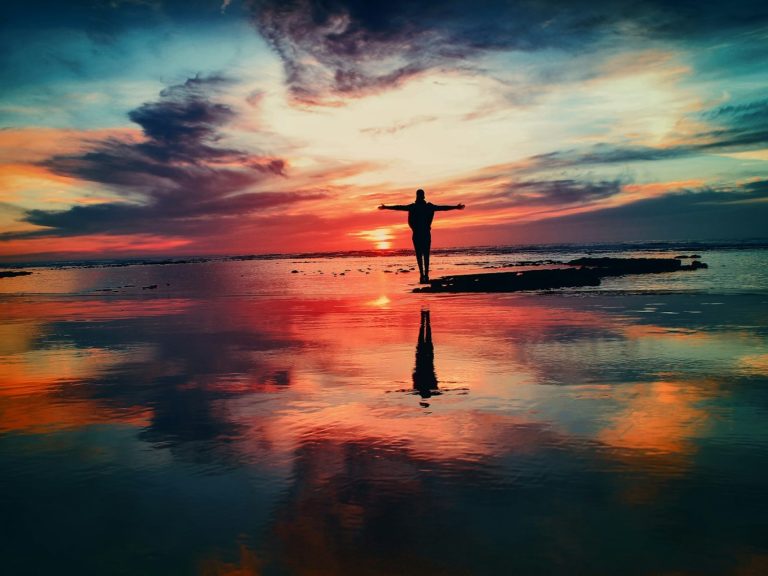 silhouette of person standing on rock surrounded by body of water